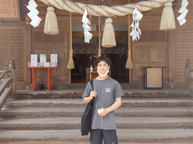 A man standing in front of steps leading up to a building, with a large rope and tassels hanging over the doorway
