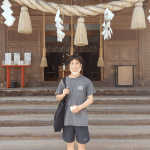 A man standing in front of steps leading up to a building, with a large rope and tassels hanging over the doorway