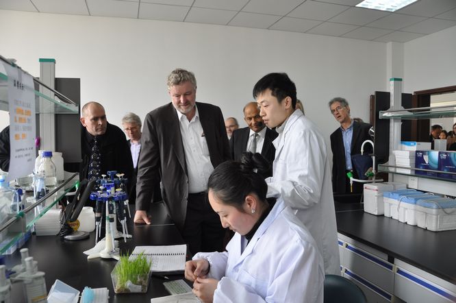 A young Chinese researcher explains to delegation members the work being done by a lab-coated female colleague.