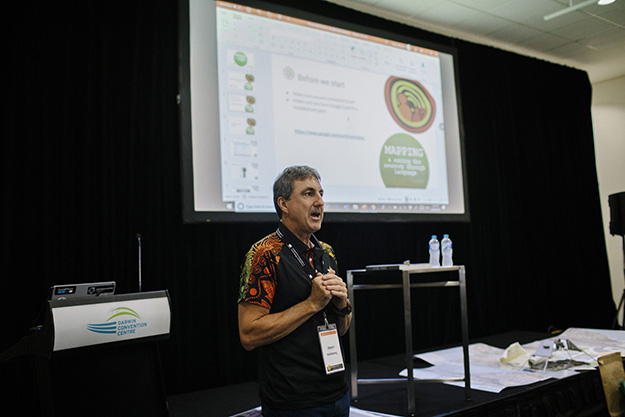 A First Nations man presents in front of a PowerPoint presentation in a corporate environment.