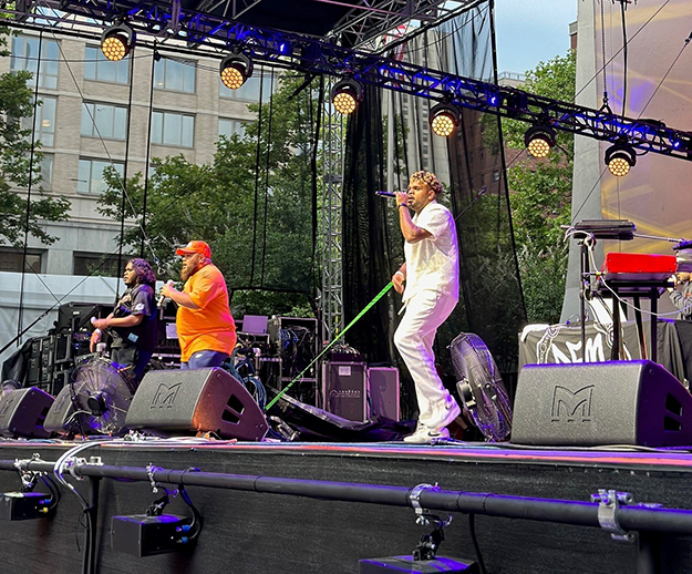 Two male singers and a male guitarist perform on an outdoor stage.