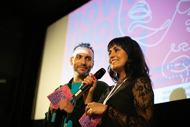 A woman smiles while presenting on a stage with her male colleague.