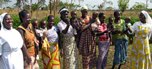 Seven Ugandan mothers standing outside holding newborn babies with a nurse standing on the left hand side.