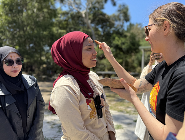 Australian indigenous woman marking the forehead of a woman with paint.