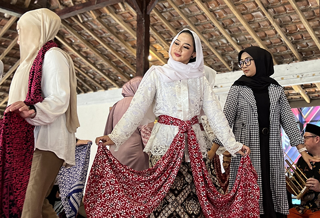 Three women wearing traditional Indonesian attire learning a dance.