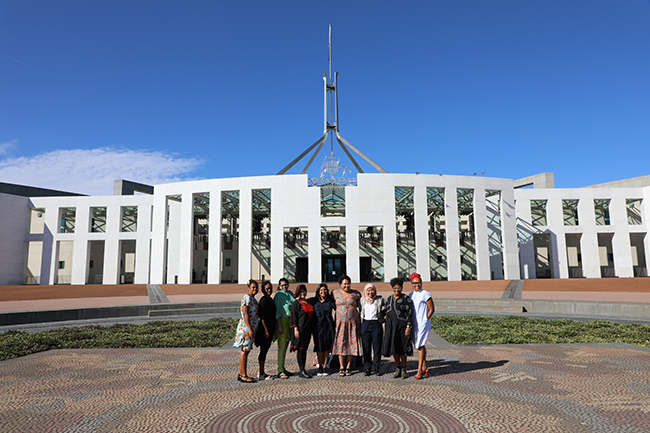 Nine women standing together in front of Parliament House in Canberra, Australia. 