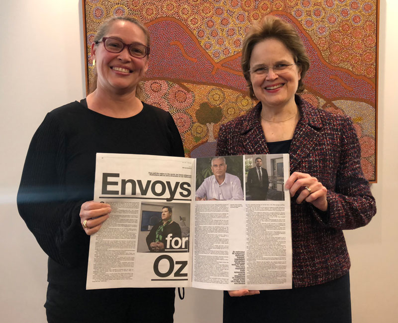 Photo of Ambassador to Madrid, Julie-Ann Guivarra and Secretary Adamson holding up a newspaper titled Envoys for Oz and has a photo of Assistant Secretary Damien Miller in it.