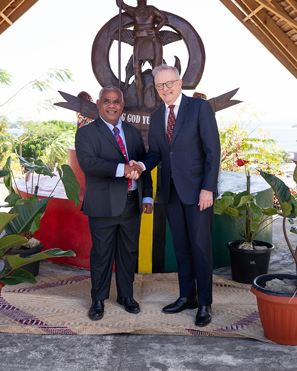 Two men standing together shaking hands, with a bronze statue in the background.