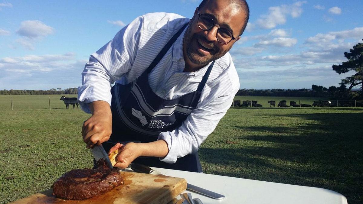 Chef Tarek cutting meat on a table out in a field.