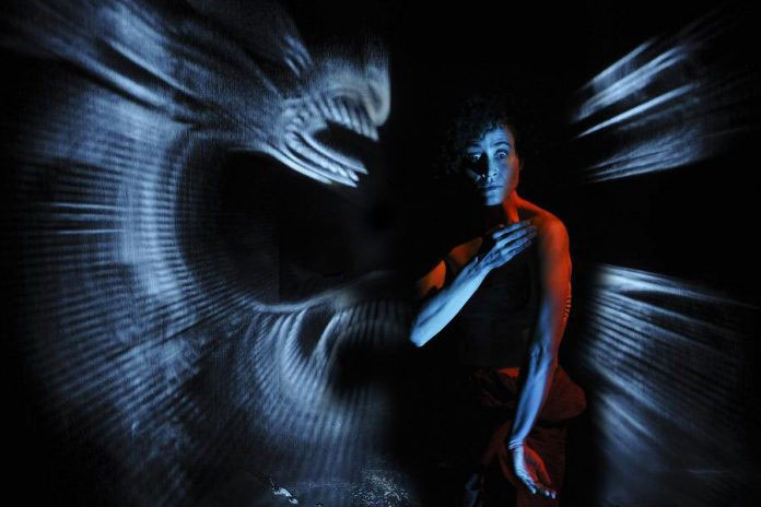 Image of Australian dance artist Victoria Hunt, performing on stage with Maori lighting projector. 