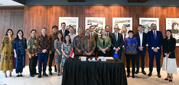 A large group of people standing inside, behind a small table with documents laid out. Indonesian and Australian flags are on display.