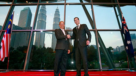 Two men standing between a Malaysian flag and an Australian flag.