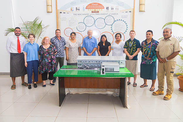 Several men and women standing behind an architectural model of a building.