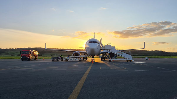 Aircraft sitting on a runway being loaded with luggage. A fuel truck is parked off to the side.