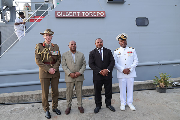 4 men standing in a row in front of a guardian class patrol boat