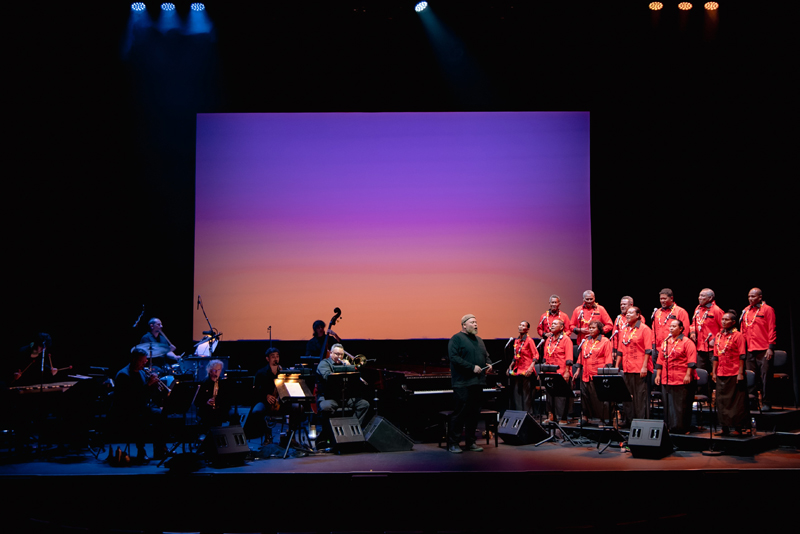 Musicians on stage with a choir wearing bright red shirts.