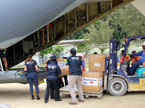 A forklift carrying boxes of Australian Aid and officials loading it into the back of an airplane.