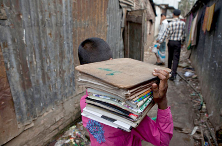 Child walking through alley carrying books on his shoulder