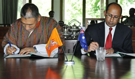 Bhutan's Ambassador to India with the Australian Ambassador to Bhutan signing the agreement. On the table are two miniature flags of Bhutan and Australia