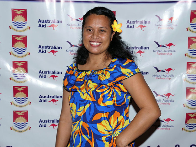 A woman in colourful clothing standing in front of an Australian Aid  and Kiribati-Australia Partnership backdrop