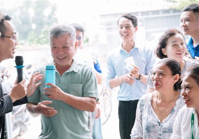 Mr Duy (surrounded by onlookers) holding a bottle of purified water in his hand with a big smile.