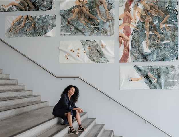 Person sitting on steps with artwork on the wall behind