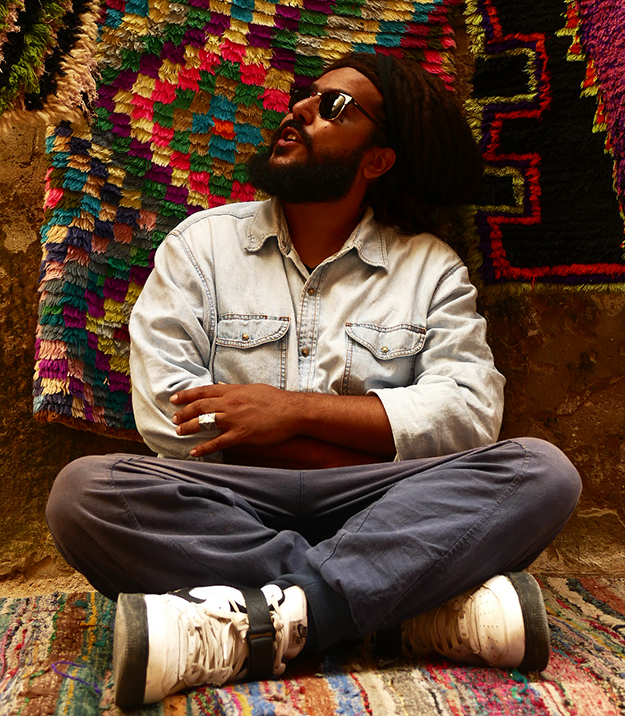 Person sitting crossed legged looking up at a colourful rug hanging on the wall behind them.