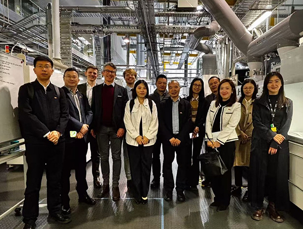Aa large group of people touring inside an industrial facility surrounded by a large system of inter-connecting pipes and machinery.