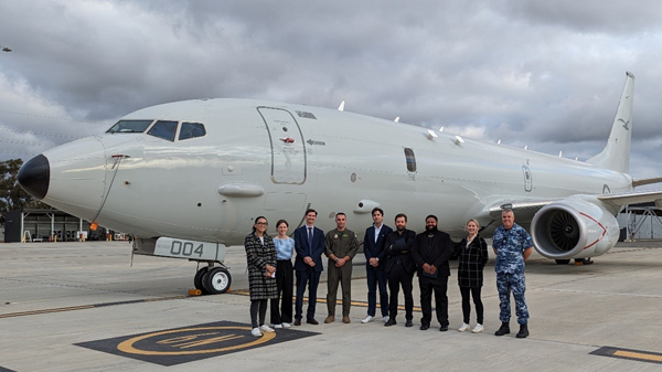 Nine people standing on a tarmac in front of a plane.