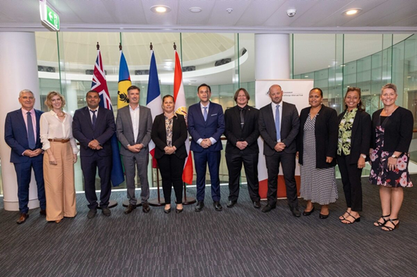 Five women and 6 men standing in front of flags from the countries of Australia, French Polynesia, New Caledonia.