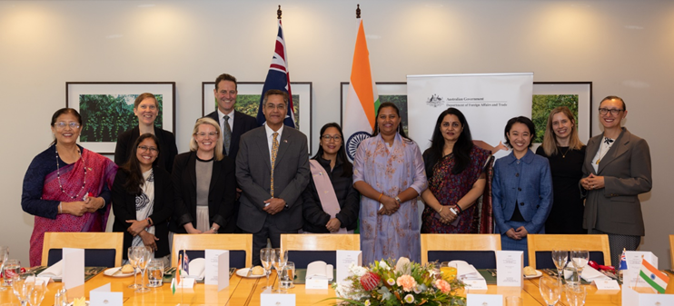 10 women anfd 2 man standing in front of a table with the flags of Australia and Inda behind.