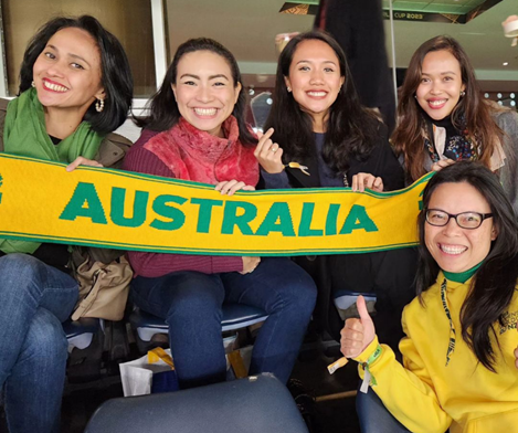 5 women holding a green and gold scarf with "Australia" written across it