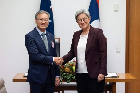 Man and women shaking hands in front of a table with the flags of Australia and Laos in the background.