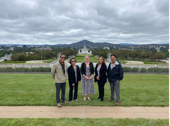 5 people standing on the lawns of parliament house, wit hold parliament house and mountains in the background.