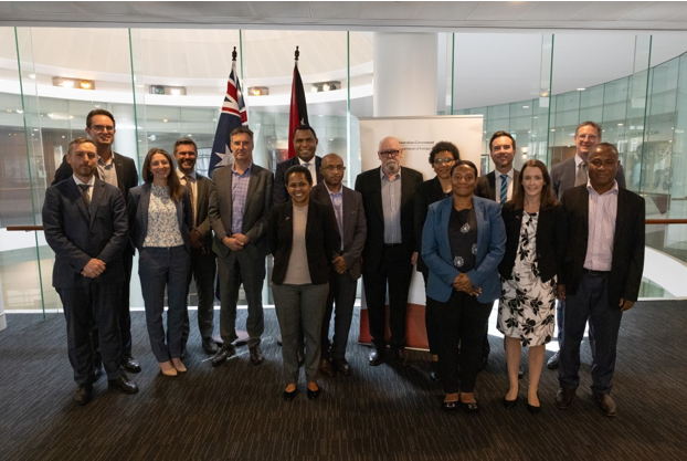 15 delegates from Australia and PNG standing in a row in front of the flags of Australia and PNG.