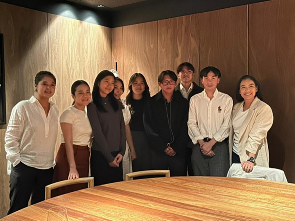 6 women and 3 men from Thailand standing in a group in front of a table.