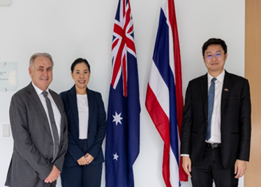 2 men and a women standing next to the flags of Australia and Thailand