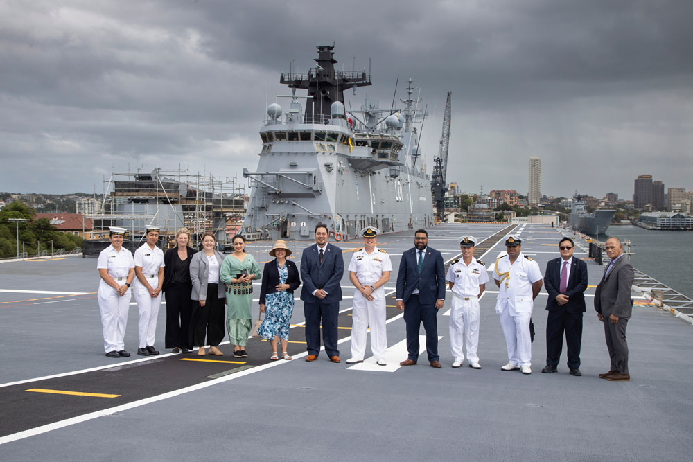 A group photo on the docks at Fleet Base East, a large ship in the background. In the centre are His Royal Highness, Crown Prince of Tonga Tupouto'a 'Ulukalala and Rear Admiral Christopher Smith, with delegates and members of the Royal Australian Navy.