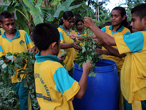 6 children holding working with branches around a barrel container