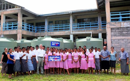 Group of people standing in front water tanks with a an Australian aid logo on them