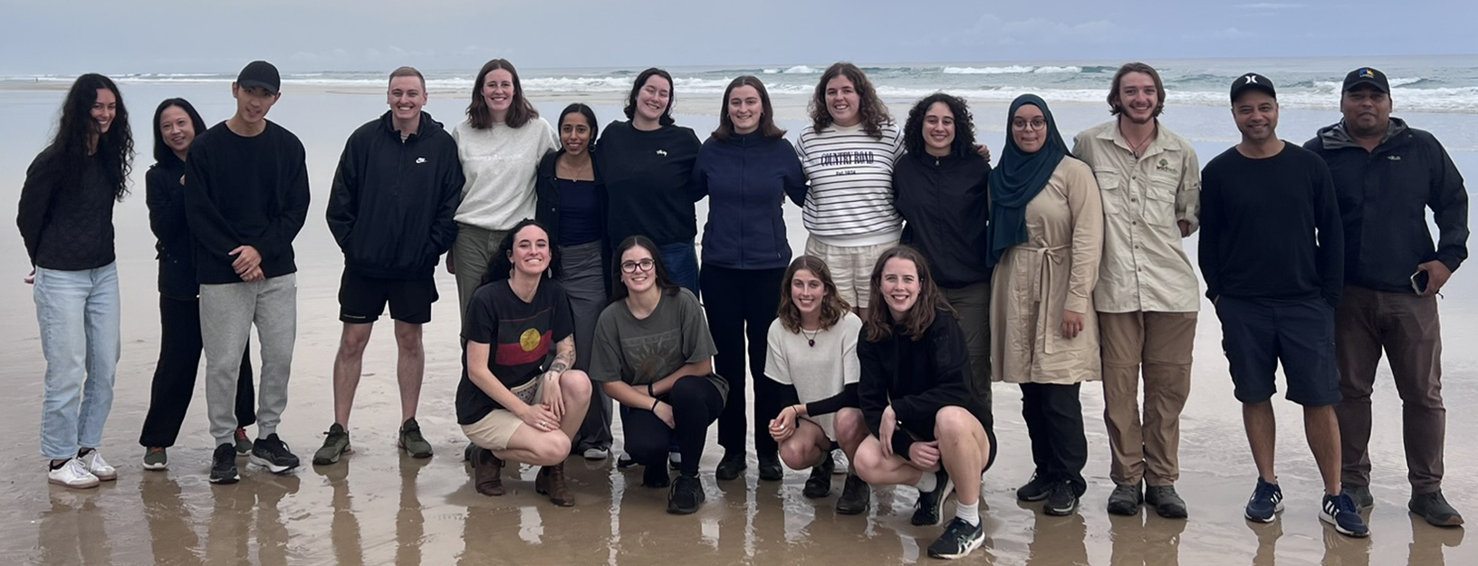 Group shot of Lyndon with New Colombo Plan scholars on a beach with the sea and sky in the background