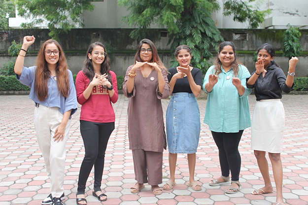 six women standing together making signs with their hands.