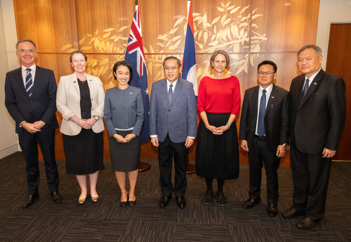 Seven people stand in a row in front of Australian and Lao flags