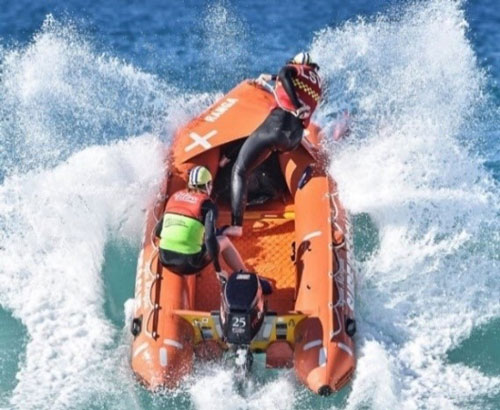 Photo of two life savers in an inflatable rescue boat going over a wave in the ocean.