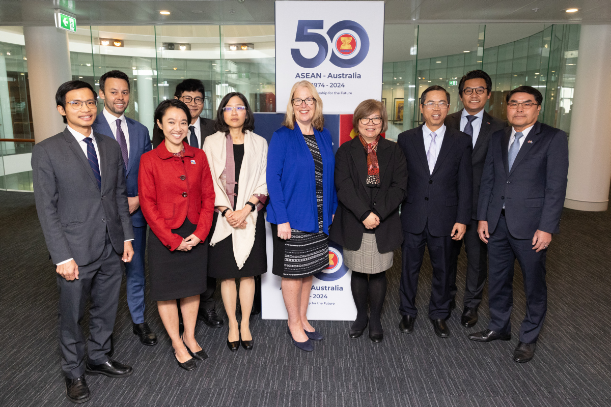 Ten people stand in a group in front of a banner commemorating the 50th anniversary of ASEAN-Australia dialogue relations.