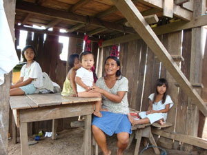 Young Filipino family sitting in a wooden hut. Mother is sitting in front resting baby on table. Three young girls are sitting in the background.