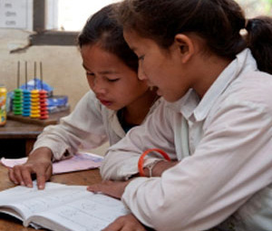 Class room full of children reading books together. Background walls are decorated with colourful papers. A blue lantern hangs from the ceiling.