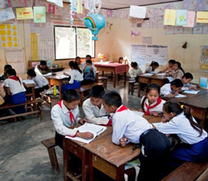 Two young schoolchildren from Laos are sitting at a table reading a book together.