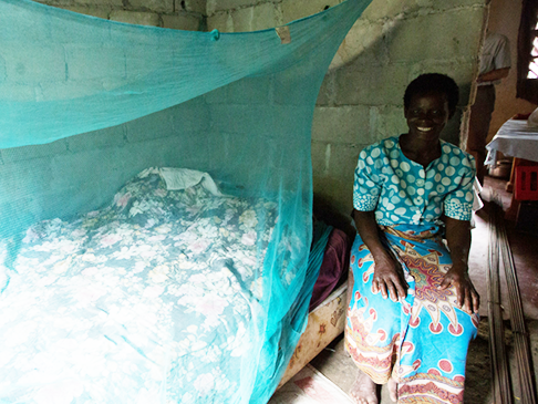 Woman sitting by her bed with a mosquito net hanging over it