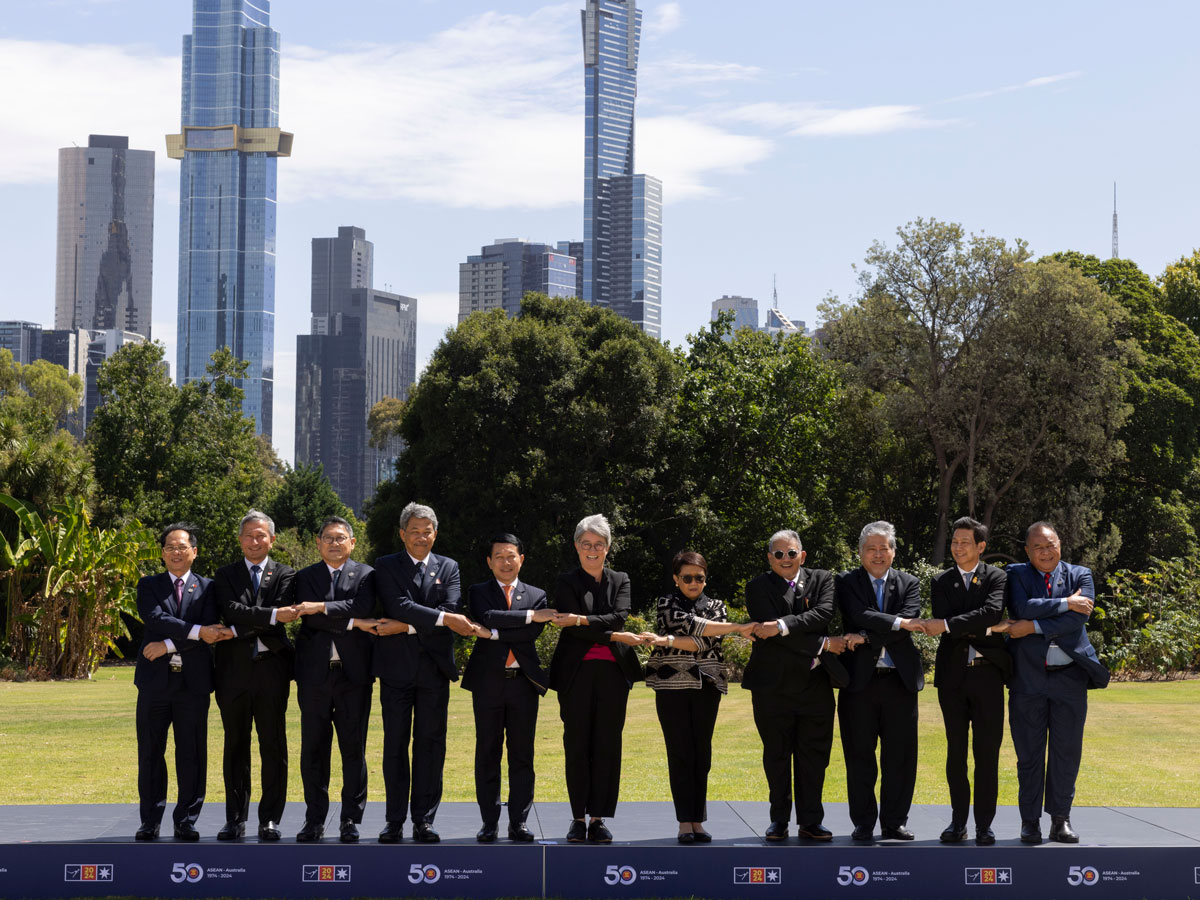 Eleven people stand on a podium against the backdrop of Melbourne cityscape, shaking hands through crossed and joined arms.